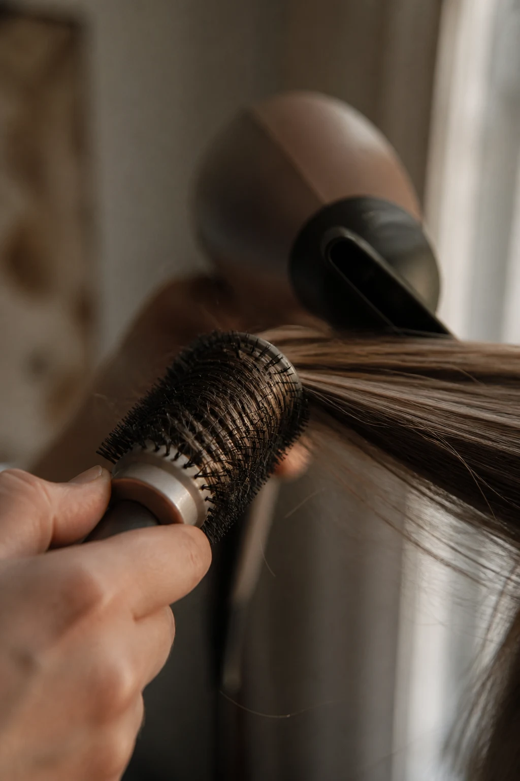 A round brush lifting a section of hair mid-blowout